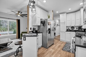 A modern kitchen with white cabinetry, a stainless steel refrigerator, and a ceiling fan. - Sunset View Cottage - Brand new home on the Bluff (Moclips)