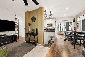 Uma sala de estar moderna com televisão de tela plana, uma mesa de centro de madeira e um espaço de jantar com mesa e cadeiras.
