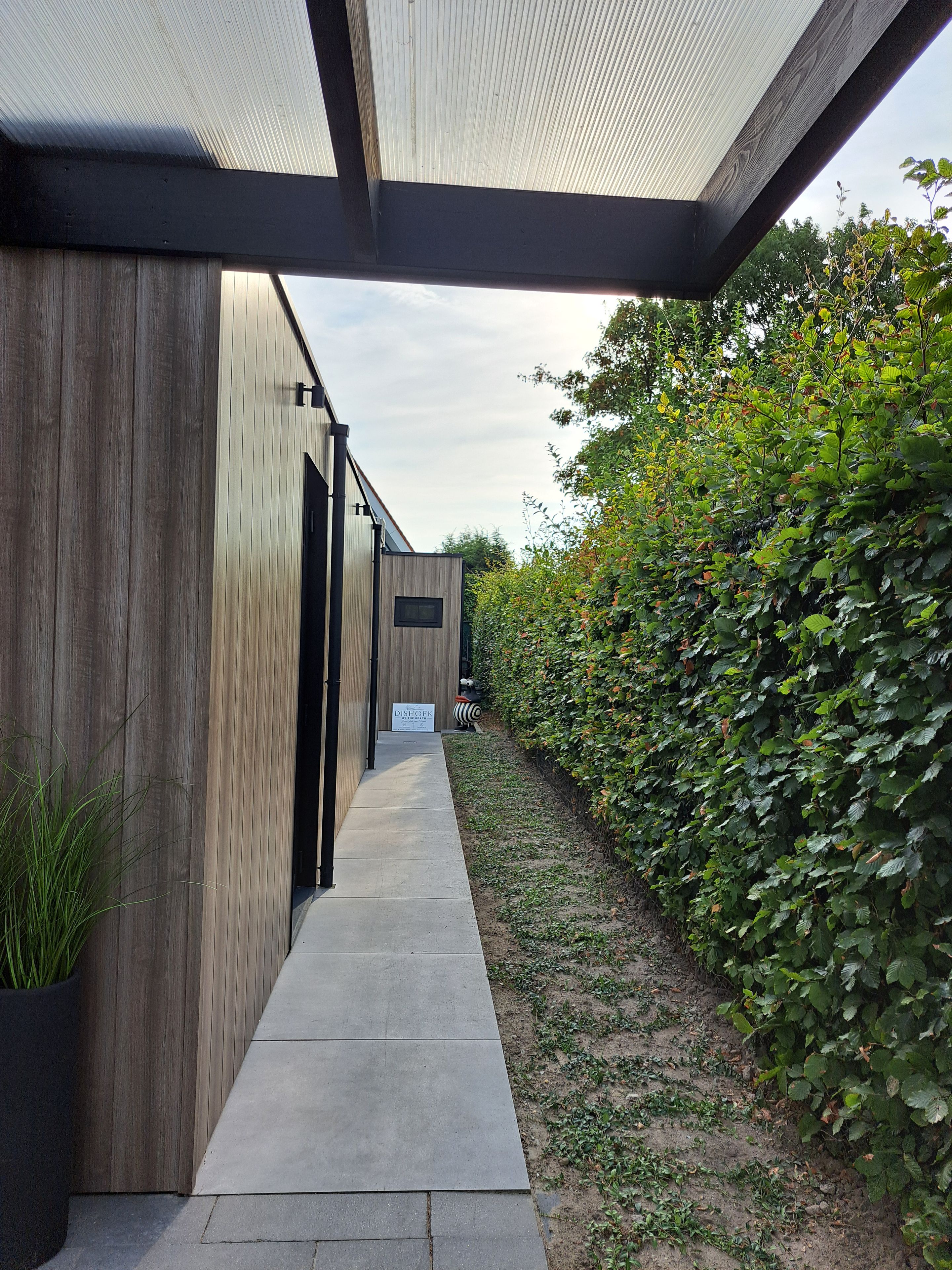 A modern building with a covered walkway, wooden siding, and a signboard.