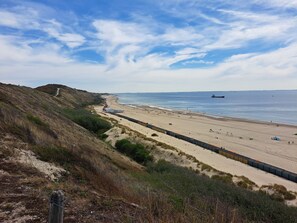 A coastal landscape with a sandy beach, a road leading to a building, and a ship in the distance. - Adorable 1-bedroom cottage with AC in charming Dishoek (Koudekerke)