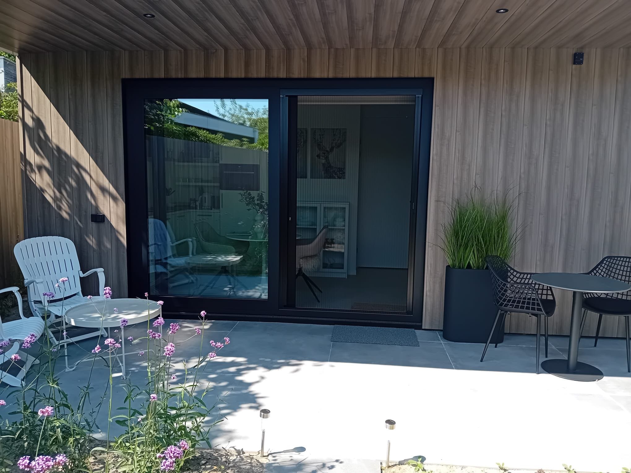 A modern patio with a glass door leading to a covered area, outdoor furniture, and a potted plant.