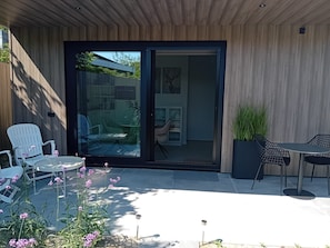 A modern patio with a glass door leading to a covered area, outdoor furniture, and a potted plant.