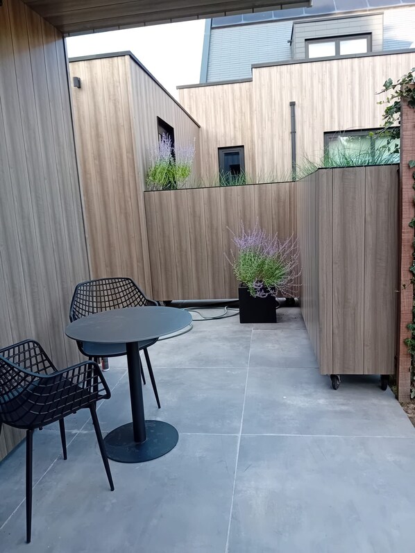 An outdoor patio with a round table and two chairs, a wooden fence, and potted plants.