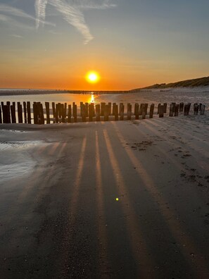 Ein Strand mit einer Holzlattenveranda und einem Steg im Hintergrund bei Sonnenuntergang.