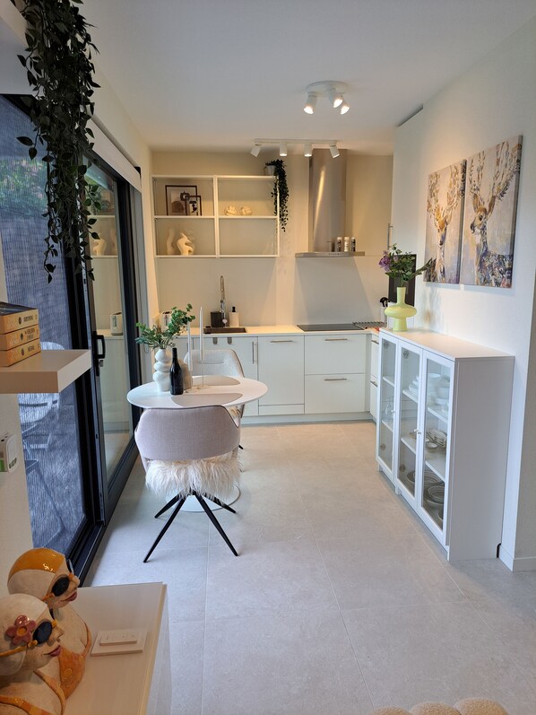 A modern kitchen with white cabinetry, a round table with a fluffy chair, and a glass cabinet with dishes.