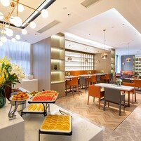 Un comedor moderno con sistema de buffet, que incluye frutas y verduras, y un espacio de asientos con mesas y sillas.