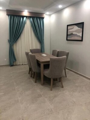 Un comedor con una mesa redonda y seis sillas, cortinas y un cuadro en la pared.
