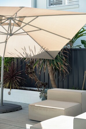 An outdoor seating area with a large umbrella, a sofa, and various plants. - "Bluewater" – Pool at home, Beach just beyond (North Avoca)
