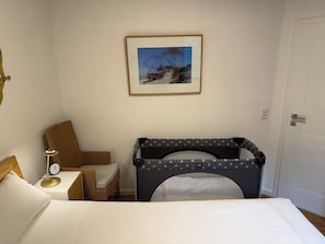 A room with a bed, a chair, a small table with a lamp, a crib, and a framed picture on the wall. - Comfortable vacation rental for up to 4 people, 2 bedrooms, quiet, green setting, west-facing terrace, Wi-Fi, 4-star DTV (Ostseebad Prerow)