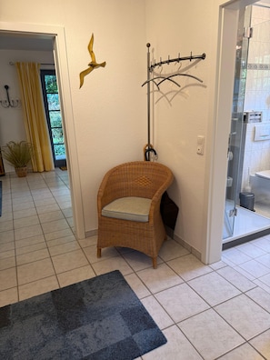 A corner of a room with a wicker chair, a black rug, and a wall-mounted drying rack. - Comfortable vacation rental for up to 4 people, 2 bedrooms, quiet, green setting, west-facing terrace, Wi-Fi, 4-star DTV (Ostseebad Prerow)