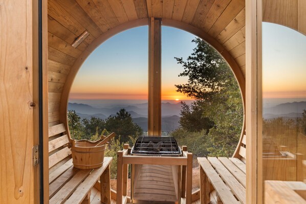 A wooden cabin with a circular window overlooking a mountainous landscape during sunset.