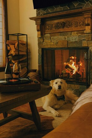 Una habitación acogedora con chimenea, un perro acostado en el suelo y una mesa con una botella y vasos.