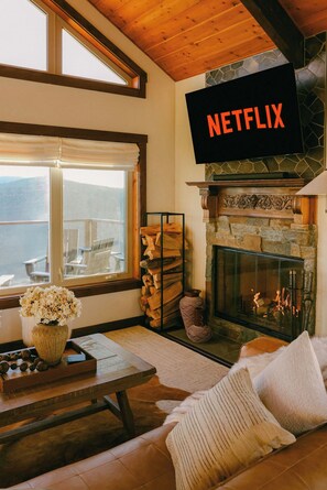 Una sala de estar acogedora con chimenea, un letrero de Netflix, un sofá y vistas al exterior.