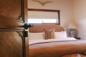 A hotel room with a bed, a nightstand, a lamp, and a window with blinds.