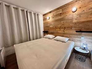 A bed with a white bedspread, two pillows, and a wooden headboard with built-in lighting. - Plagne 1800, sleeps 6, renovated in 2026, pool, sauna, covered parking. (La Plagne Tarentaise)