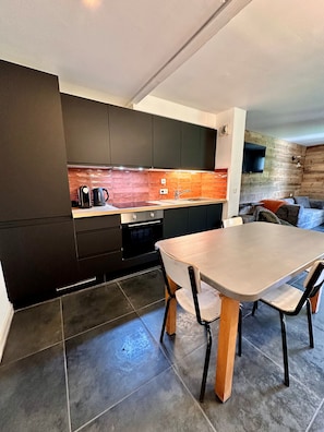 A modern kitchen with dark cabinetry, a wooden dining table, and a stone backsplash. - Plagne 1800, sleeps 6, renovated in 2026, pool, sauna, covered parking. (La Plagne Tarentaise)