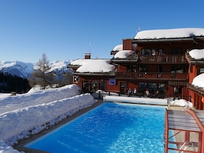 A hotel with a pool surrounded by snow, a mountain view, and a sign indicating a restaurant. - Plagne 1800, sleeps 6, renovated in 2026, pool, sauna, covered parking. (La Plagne Tarentaise)
