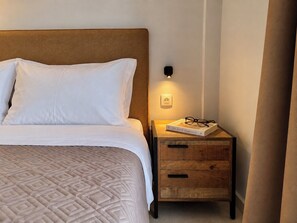 A neatly made bed with a patterned bedspread and white pillows, a wooden bedside table with a book and glasses, and a wall-mounted light. - 6th Floor Loft in the Heart of Athens ΙΙ by ΜΡS (Athina)