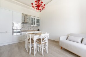 A modern kitchen with white cabinetry, a built-in oven, and a dining table with white chairs. - Ortigia Prestige | 2 bedrooms and 2 bathrooms, just a short walk from the Duomo (Siracusa)