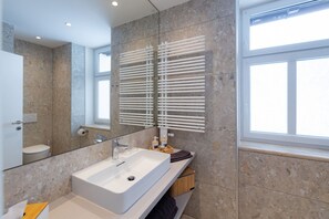 A modern bathroom with a white sink, a mirror, and a towel rack. - Cozy apartment with a balcony and a view of the garden. (Semmering-Kurort)