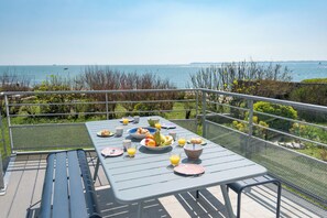An outdoor dining area with a table set for breakfast, overlooking a body of water. - Large family villa on the beach by Groom* (Larmor-Plage)