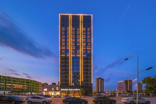 A high-rise building with illuminated vertical lines, a commercial ground floor, and surrounding urban infrastructure.