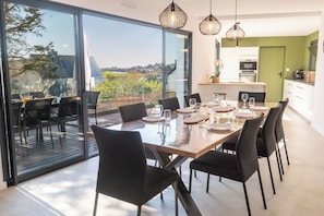 A dining area with a large table, chairs, and a view through glass doors. - Stunning premium family villa, within walking distance of the beach – by Groom* (Guidel)