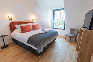A modern bedroom with a large bed, a television, and a window with a view of trees. - Stunning premium family villa, within walking distance of the beach – by Groom* (Guidel)