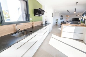 A modern kitchen with a large window, built-in appliances, and a dining area with a table and chairs. - Stunning premium family villa, within walking distance of the beach – by Groom* (Guidel)