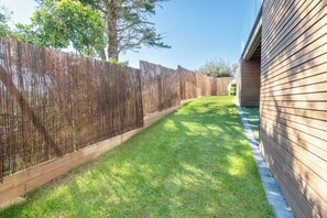 A fenced backyard with a wooden fence, a grassy lawn, and a house with horizontal siding. - Stunning premium family villa, within walking distance of the beach – by Groom* (Guidel)