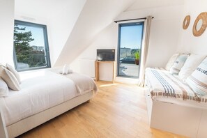 Quarto moderno com teto inclinado, uma cama, um sofá e uma TV sobre uma mesinha.