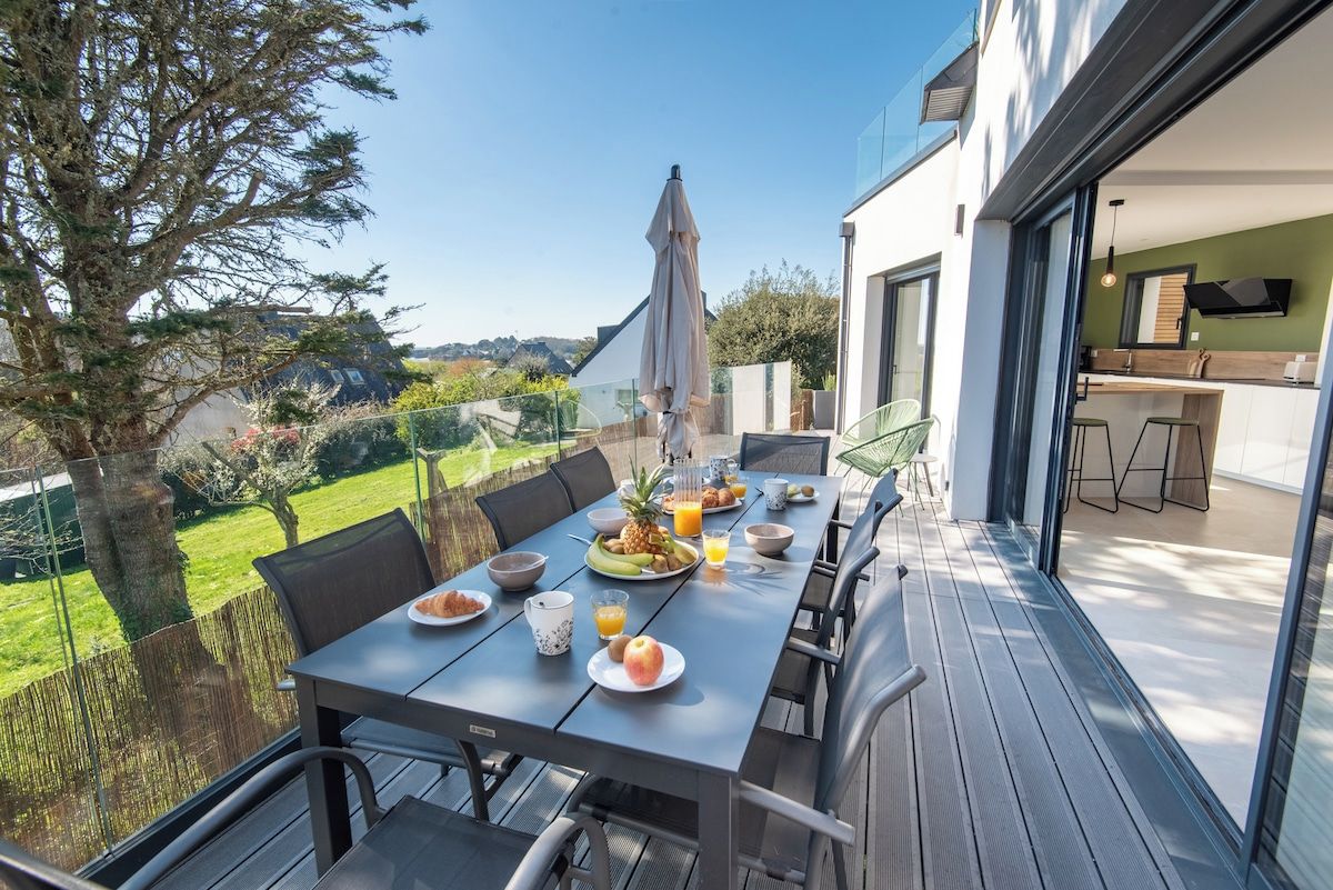 An outdoor dining area with a table set for breakfast, overlooking a garden and a modern building.
