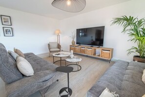 A modern living room with a grey sofa set, a flat-screen TV, a lamp, and a potted plant. - Stunning premium family villa, within walking distance of the beach – by Groom* (Guidel)