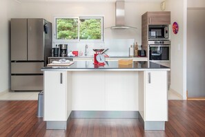 A modern kitchen with a central island, stainless steel appliances, and a view of greenery outside. - Modern beachfront house by Groom* (Larmor-Plage)
