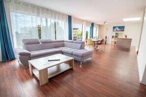 A modern living room with a sectional sofa, a coffee table, and a dining area with chairs and a table. - Modern beachfront house by Groom* (Larmor-Plage)