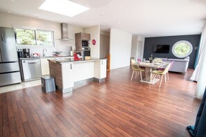 A modern kitchen with a central island, built-in appliances, and a dining area with a round table and chairs. - Modern beachfront house by Groom* (Larmor-Plage)