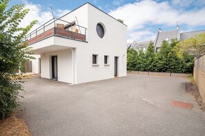 A modern two-story building with a flat roof, a balcony on the upper floor, and a circular window on the facade. - Modern beachfront house by Groom* (Larmor-Plage)
