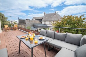 A rooftop terrace with a dining table, a sofa, and a view of the cityscape. - Modern beachfront house by Groom* (Larmor-Plage)