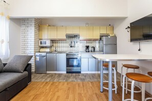 Una cocina compacta con electrodomésticos modernos, un comedor con taburetes y un sofá gris.