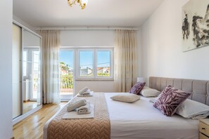 Un dormitorio con cama, mesita de noche, ventana con cortinas y vistas al exterior.