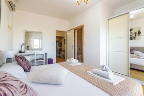 Ein Hotelzimmer mit Bett, Schreibtisch, Spiegel, Kleiderschrank und einem durchgehenden Türspalt sichtbaren Badezimmer.