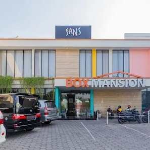 A building with a sign reading 'BOX MANSTON' and a parking area with several cars and motorcycles. - Sans Hotel Box Mansion Surabaya (Surabaya)