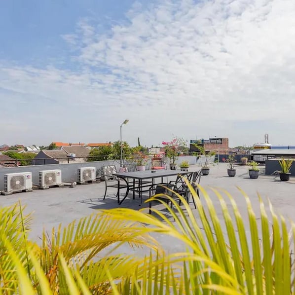 A rooftop terrace with a table and chairs, surrounded by potted plants and air conditioning units. - Sans Hotel Box Mansion Surabaya (Surabaya)