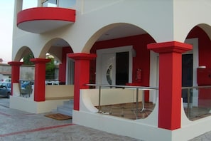 A building with red and white exterior, a glass balcony, and a staircase leading to an entrance. - Valena Studios Apartments (Lefkada)