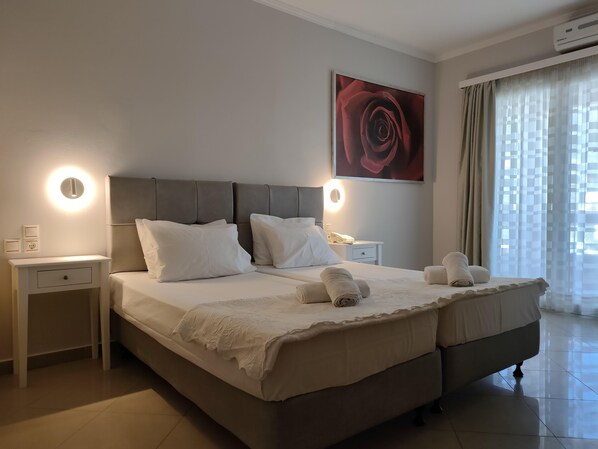 A double bed with a headboard, bedside tables, a wall-mounted artwork, and a window with curtains. - Valena Studios Apartments (Lefkada)