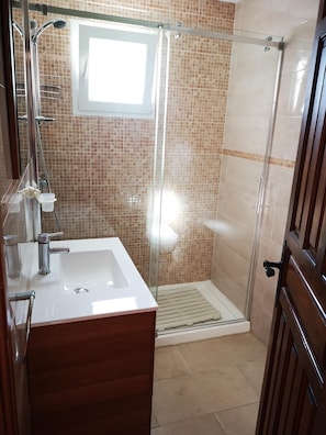 Un baño con cabina de ducha de vidrio, un lavamanos blanco y un mueble de tocador de madera.