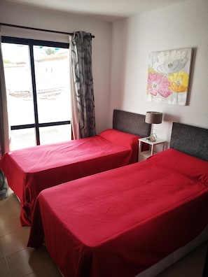 A room with two beds, a window with curtains, a small table with a lamp, and a painting on the wall. - El Capistrano Village Nicosol (Nerja)