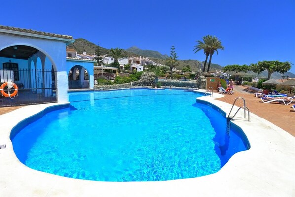 Una piscina azul cristalina con un flotador salvavidas, rodeada por un deck blanco y un muro de piedra.