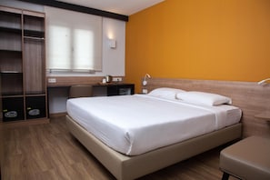 Una habitación de hotel con una cama, un escritorio, una silla y un armario.