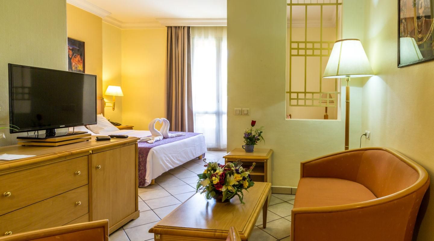 A hotel room with a bed, a TV, a desk, a chair, and a lamp.